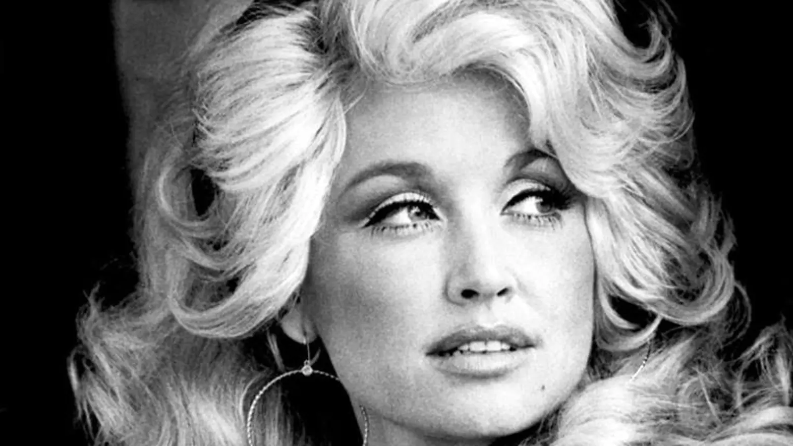 Dolly Parton posa con camisa de mezclilla en un retrato promocional en blanco y negro de 1977.
