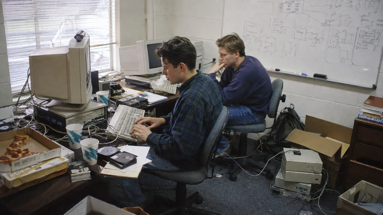 Dos emprendedores trabajando en una pequeña oficina tecnológica durante el nacimiento de Hotmail en 1996.