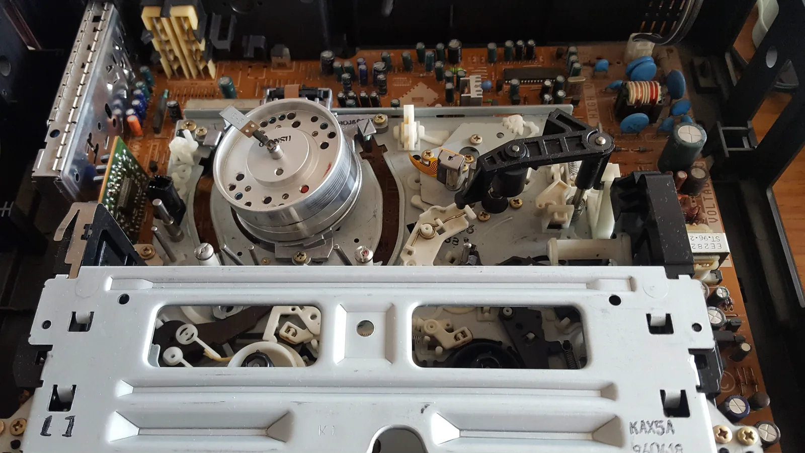 Mecanismo interno de una videocasetera VHS con engranajes, cabezal y placa electrónica visibles.