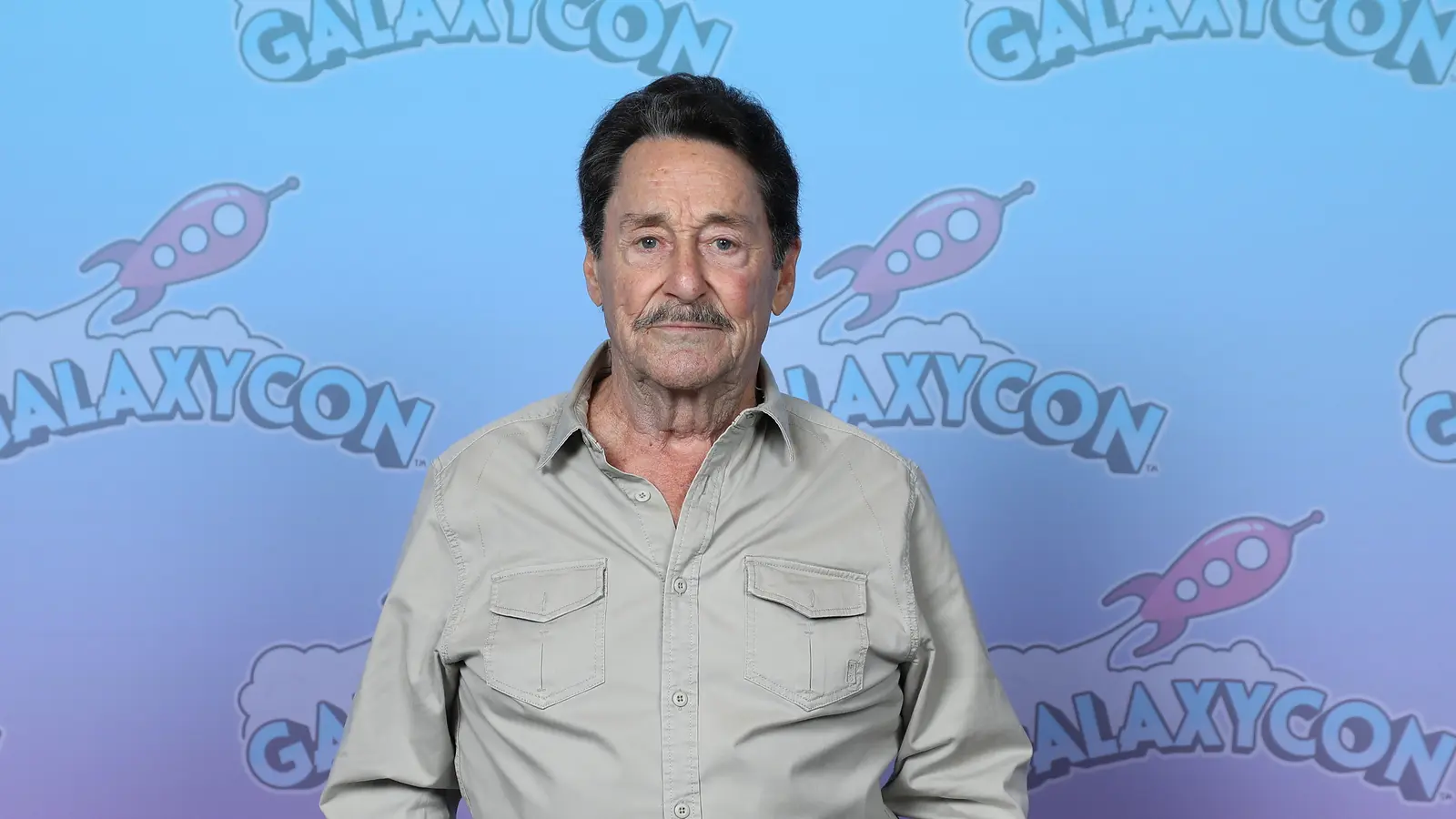 Peter Cullen posa frente al fondo de GalaxyCon Raleigh en 2023.
