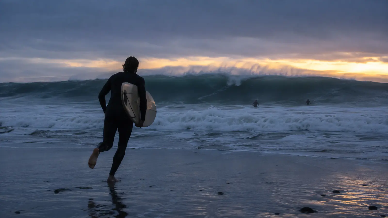 Surfista corre hacia una gran ola al amanecer con una tabla bajo el brazo.