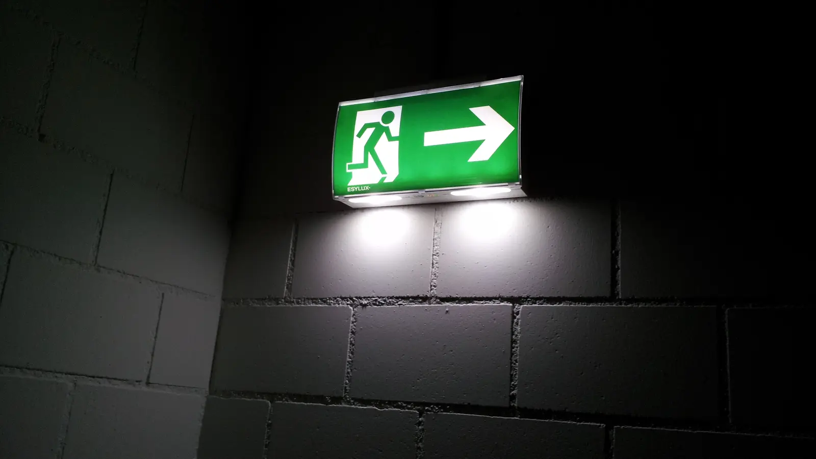 Señal verde de salida de emergencia en un pasillo oscuro