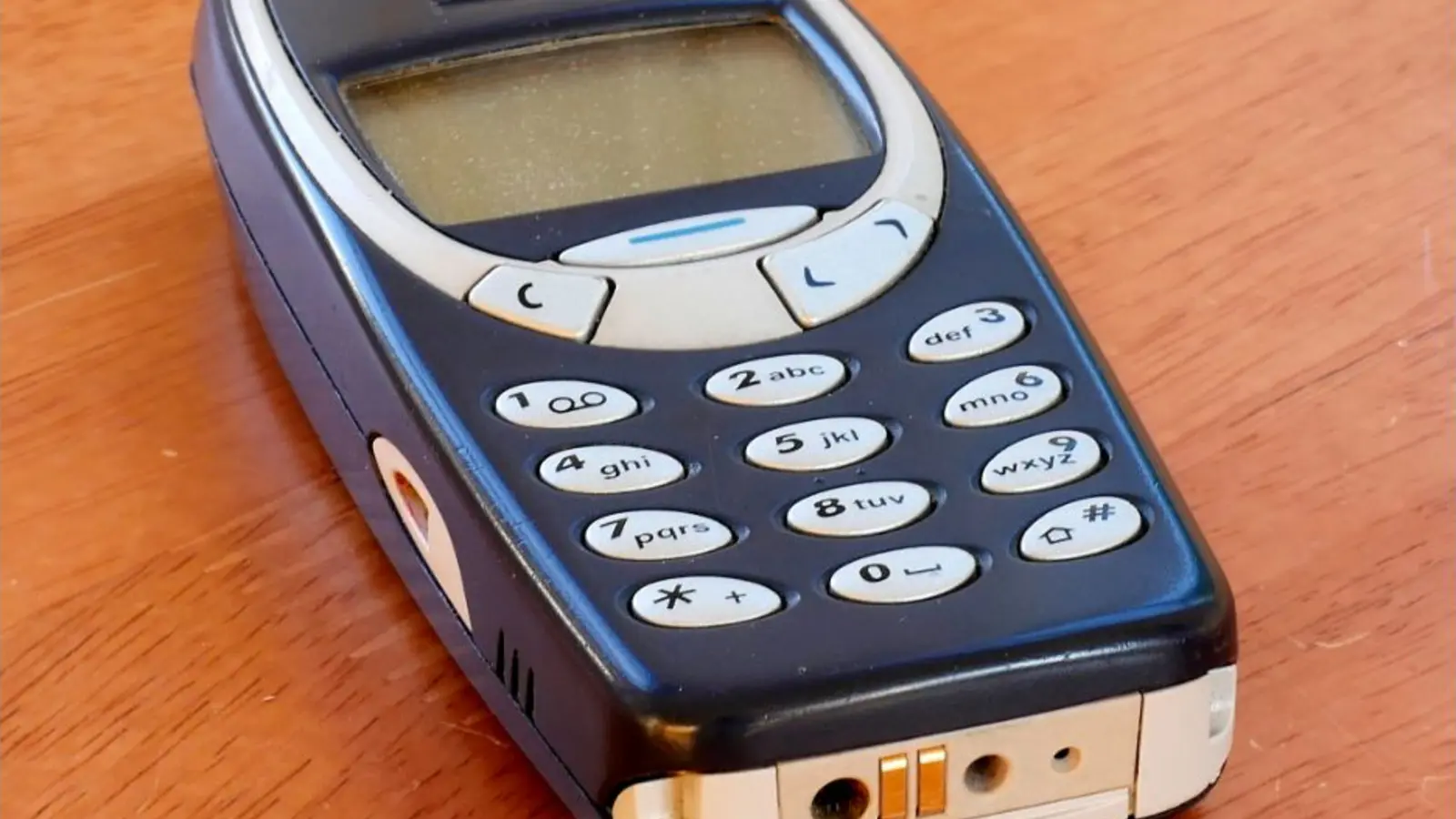 Primer plano de un teléfono Nokia 3310 azul sobre una mesa de madera.