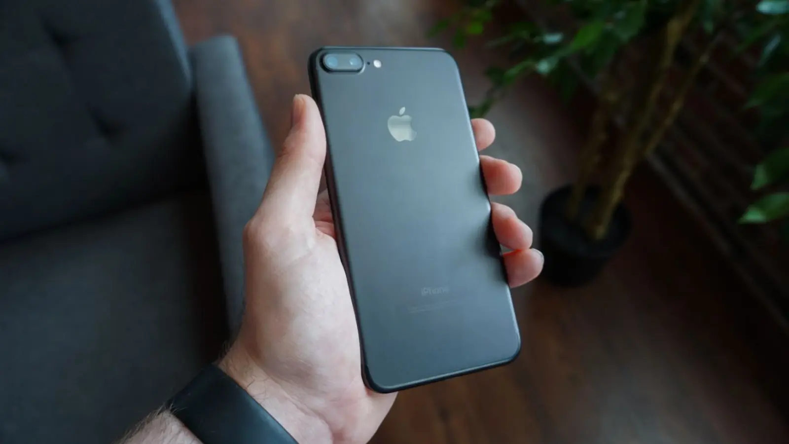 Una mano sostiene un smartphone negro en una sala moderna.